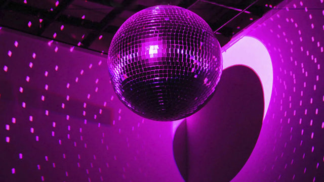 Boule à facettes en miroirs suspendue au plafond, éclairée en rose, qui projette des points lumineux sur le mur