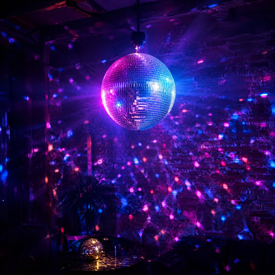 Boule à facettes argentée, suspendue dans un salon-bar sombre, qui sème des points de lumière violets, roses et cyan