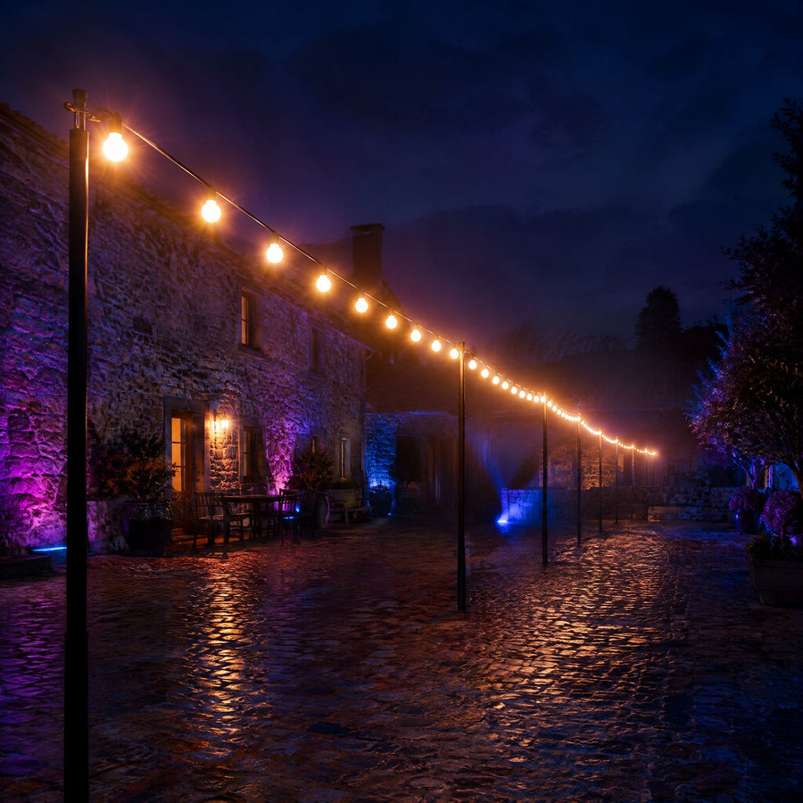Guirlande lumineuse professionnelle à globes blanc chaud tendue sur des poteaux dans la cour pavée d'une auberge