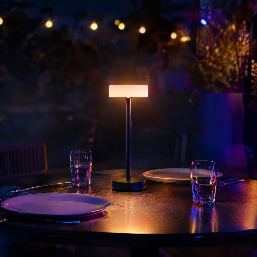 Lampe de table sans fil rechargeable noire à abat-jour givré sur une table de terrasse de restaurant à l'heure bleue