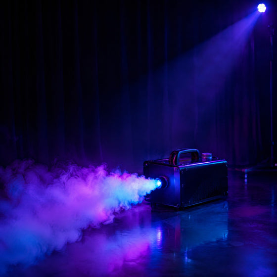 Machine à fumée noire projetant un épais brouillard éclairé en violet et cyan dans une salle de fête