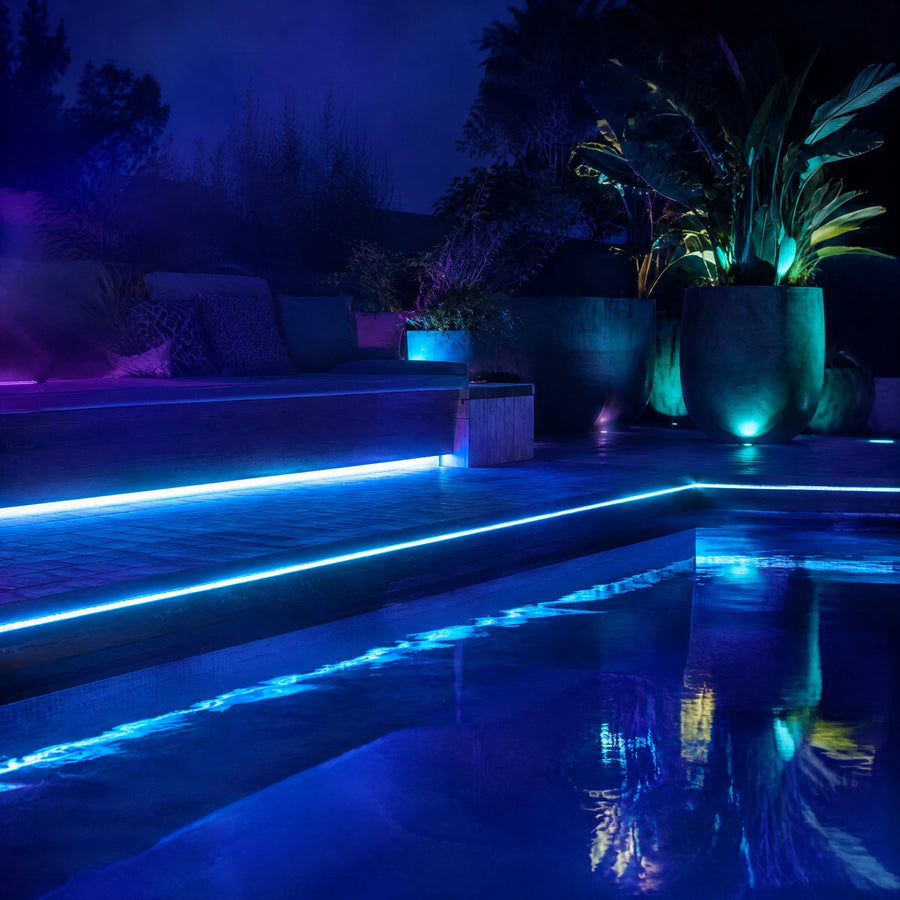 Ruban LED extérieur étanche blanc froid et cyan le long d'une terrasse en bois et sous un banc au bord d'une piscine