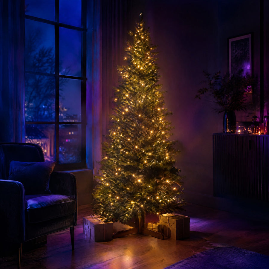 Sapin lumineux artificiel pré-éclairé en blanc chaud sur pied en bois, dans un salon près d'une grande fenêtre