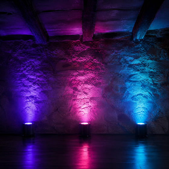 Uplights sans fil sur batterie éclairant un mur en pierre de violet, de rose et de cyan dans une grange de réception