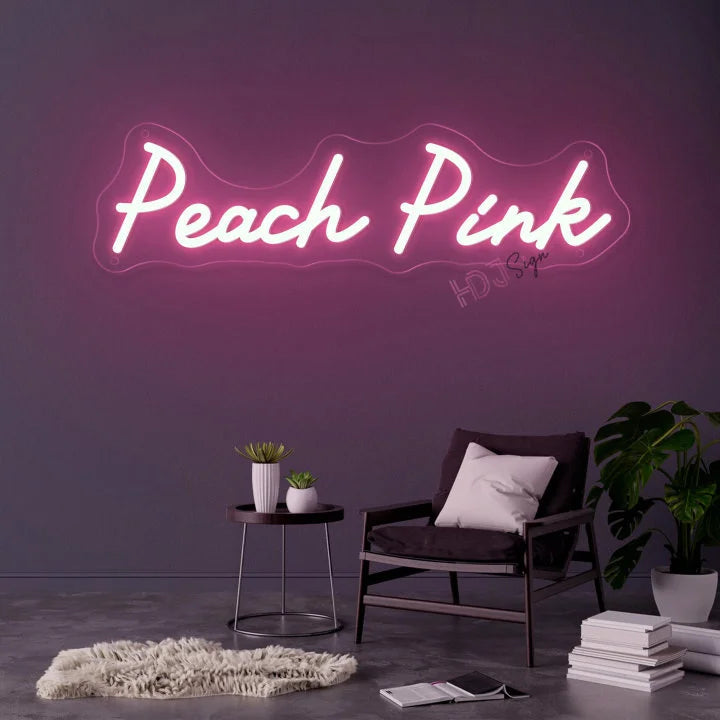 Néon prénom personnalisé cœur ou couronne – texte rose pêche sur un mur gris au-dessus d'un fauteuil