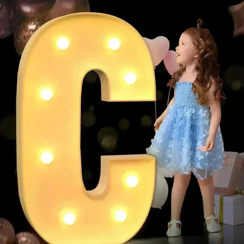 Lettre chapiteau géante – lettre C éclairée, à côté d'une fillette avec des ballons