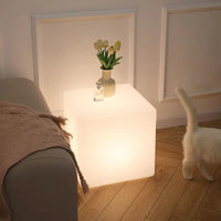 Cube lumineux LED – cube blanc chaud dans un salon, à côté d'un canapé, avec des tulipes et un flacon posés dessus
