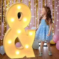 Lettre chapiteau géante – signe & éclairé, devant un décor de fête avec des ballons