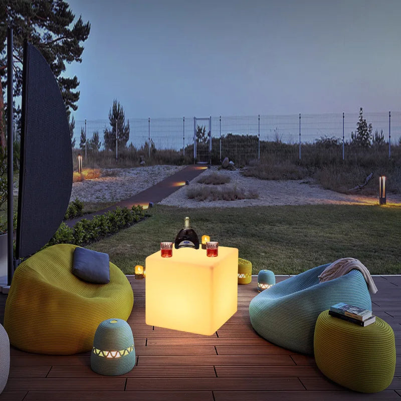 Cube lumineux LED – cube jaune sur une terrasse au crépuscule, entouré de poufs