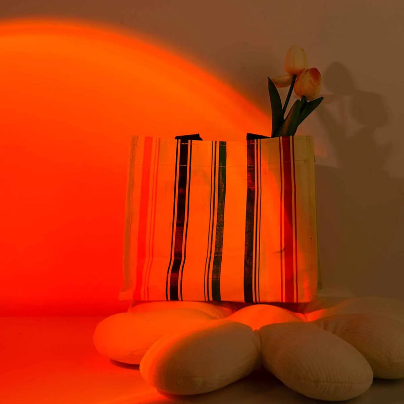 Lampe coucher de soleil sur pied 24 cm – projection orange derrière un sac et des coussins