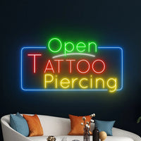 Enseigne néon Open Tattoo Piercing – au-dessus d'un canapé blanc à coussins orange