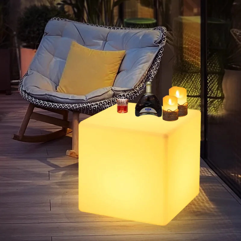 Cube lumineux LED – cube jaune près d'un fauteuil, bouteille et bougies posées dessus