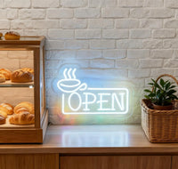Enseigne néon OPEN tasse de café – en situation dans une boulangerie près d'une vitrine de viennoiseries