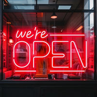 Enseigne néon We're OPEN – version rouge en vitrine d'un magasin de nuit