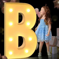 Lettre chapiteau géante – lettre B éclairée, à côté d'une fillette avec des ballons