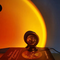 Projecteur coucher de soleil USB – posé sur un livre, halo doré sur le mur