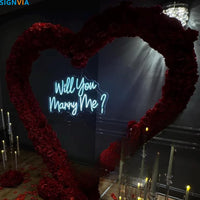 Néon Will You Marry Me – enseigne bleu glacier devant un cœur de roses rouges