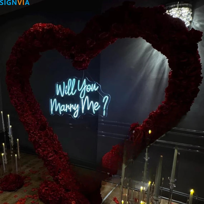 Néon Will You Marry Me – enseigne bleu glacier devant un cœur de roses rouges