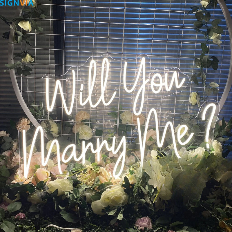 Néon Will You Marry Me – enseigne blanche devant une arche de fleurs