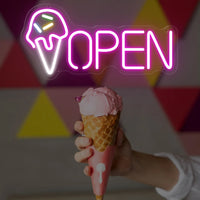 Enseigne néon OPEN cornet de glace – devant une main qui tient un cornet de glace rose