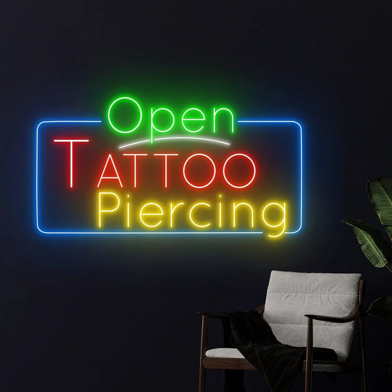 Enseigne néon Open Tattoo Piercing – sur un mur sombre à côté d'un fauteuil gris
