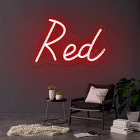 Néon prénom personnalisé cœur ou couronne – texte rouge sur un mur gris au-dessus d'un fauteuil
