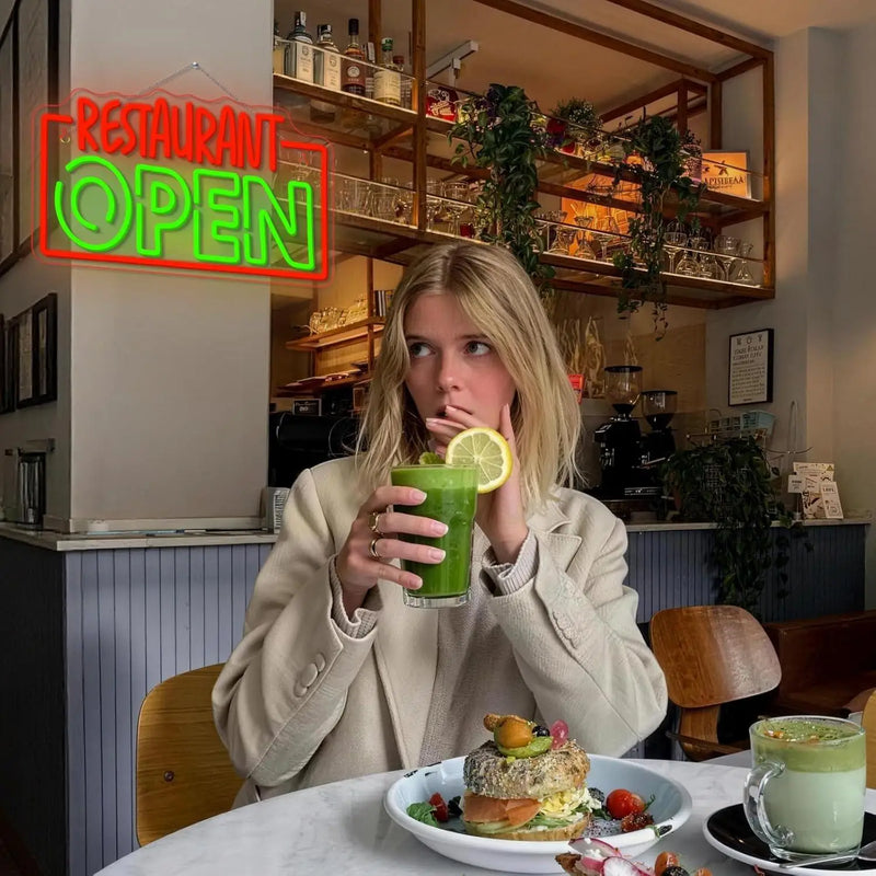 Enseigne néon RESTAURANT OPEN – dans un café, avec une cliente qui boit un jus