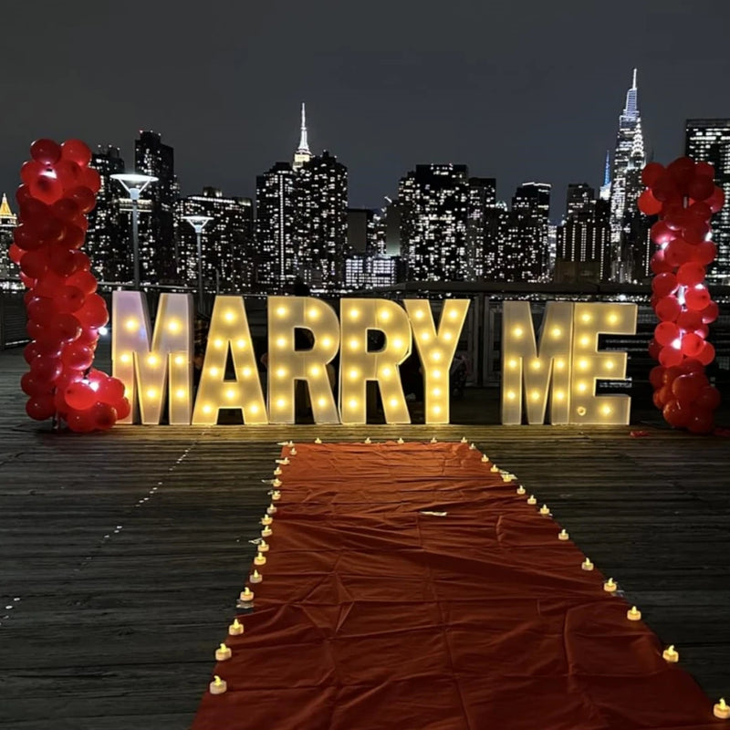 Lettre chapiteau lumineuse 91,5 cm – mot MARRY ME allumé sur une allée rouge devant une ville de nuit