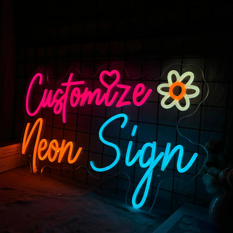 Néon personnalisé LED – exemple en écriture cursive rose, orange et bleue avec une fleur