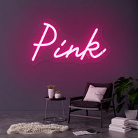 Néon prénom personnalisé cœur ou couronne – texte rose sur un mur gris au-dessus d'un fauteuil