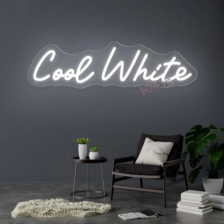 Néon prénom personnalisé cœur ou couronne – texte blanc froid sur un mur gris au-dessus d'un fauteuil