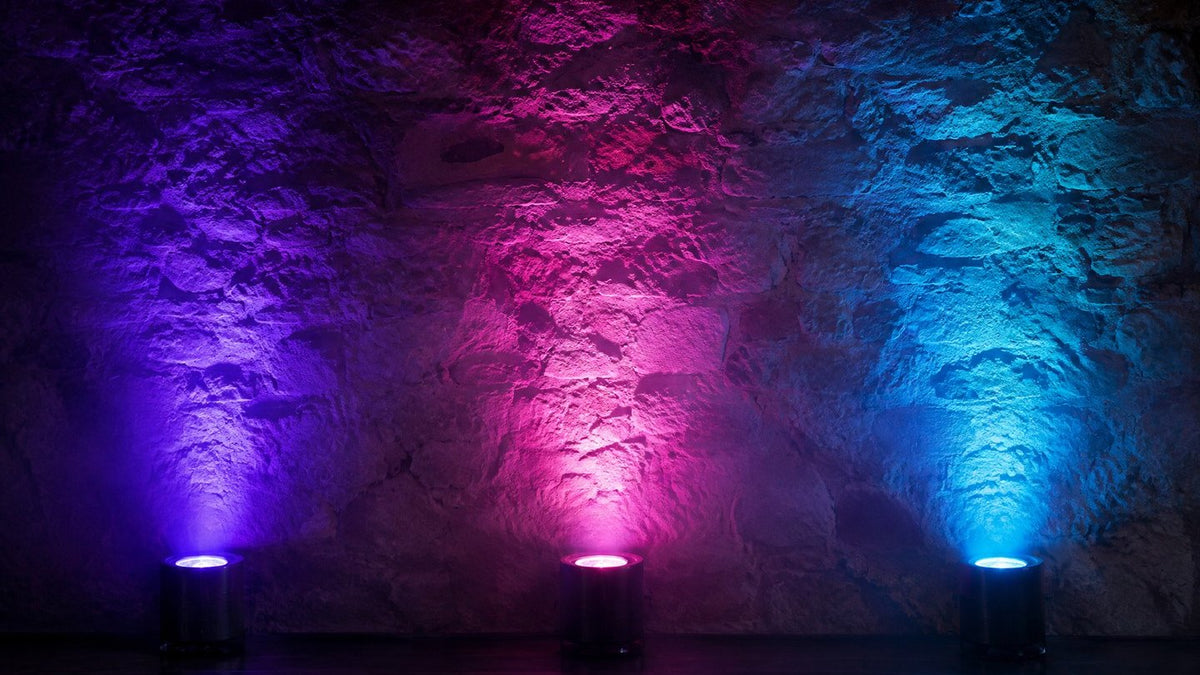 Uplights LED éclairant un mur de pierre en violet, rose et cyan